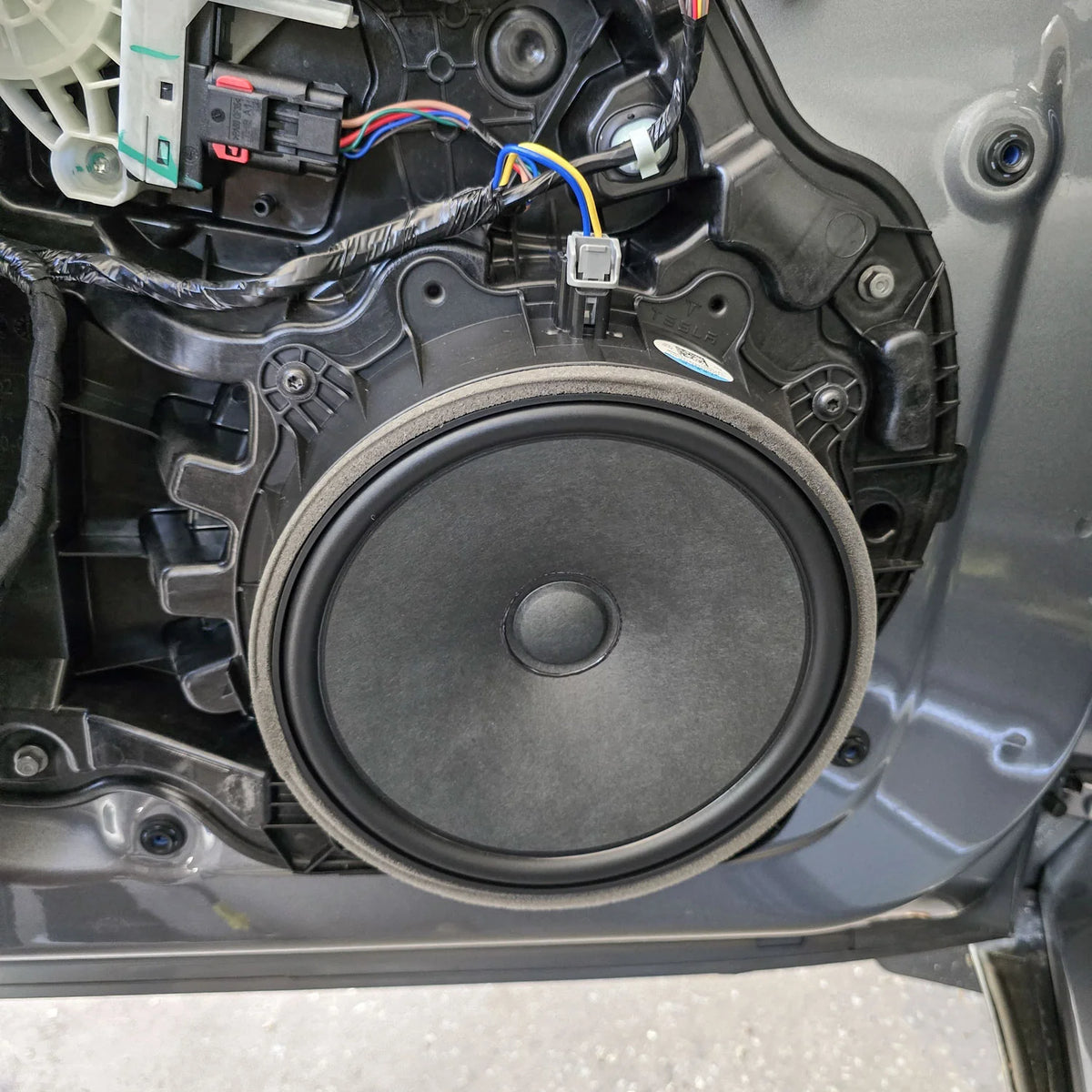 Factory Tesla Model Y door woofer shown before replacement with the HELIX Ci3 front speaker upgrade